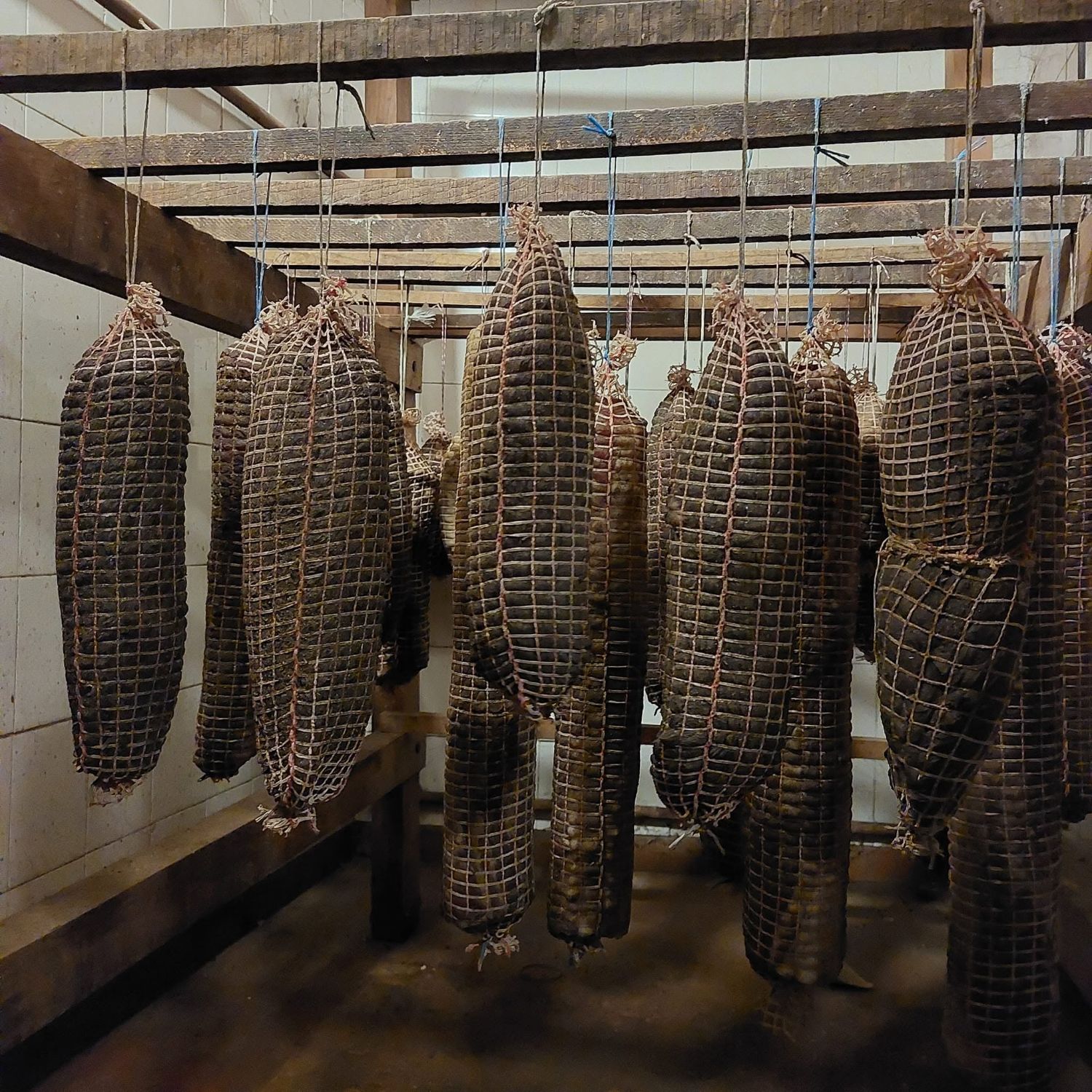 Salaisons sous filet suspendues aux poutres en bois du séchoir